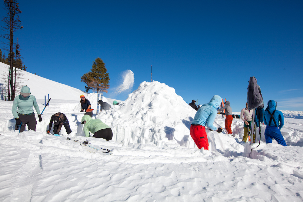 A group of winter campers shovel snow into a mound that will become a quinzhee