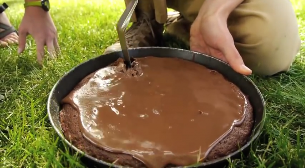 Frosted chocolate cake in a frying pan being cut by a spatula