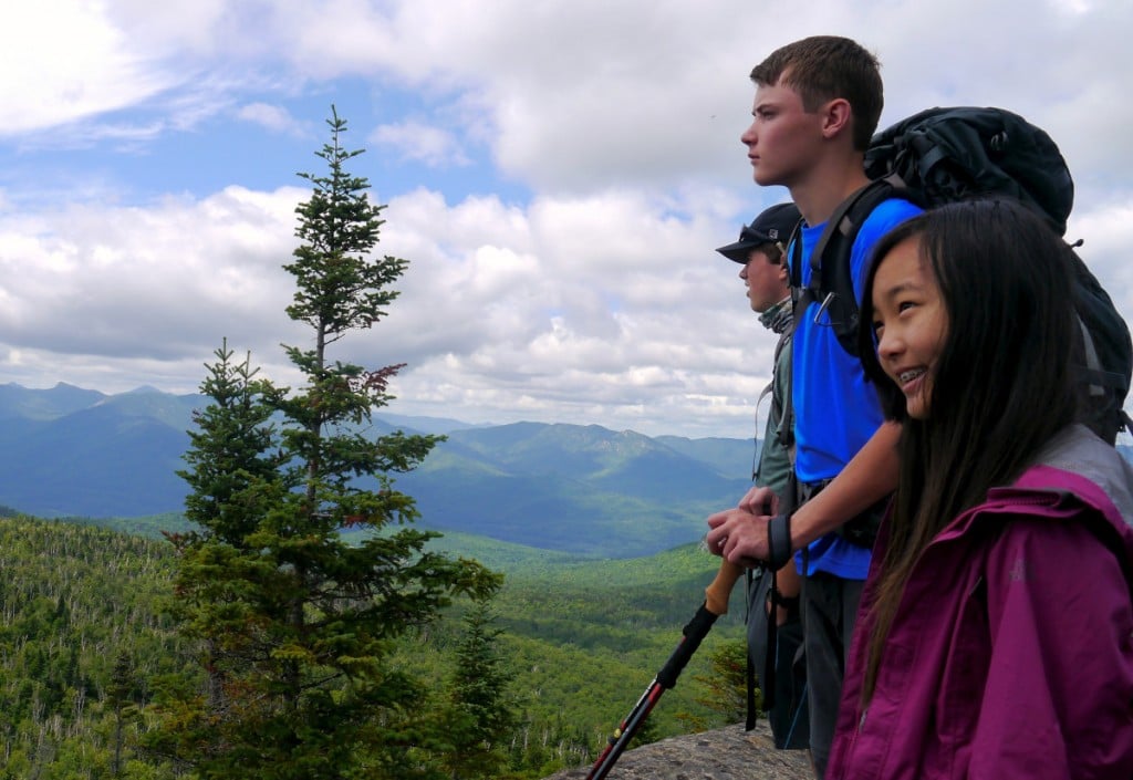 A group of teens overlooks a forested mountain valley