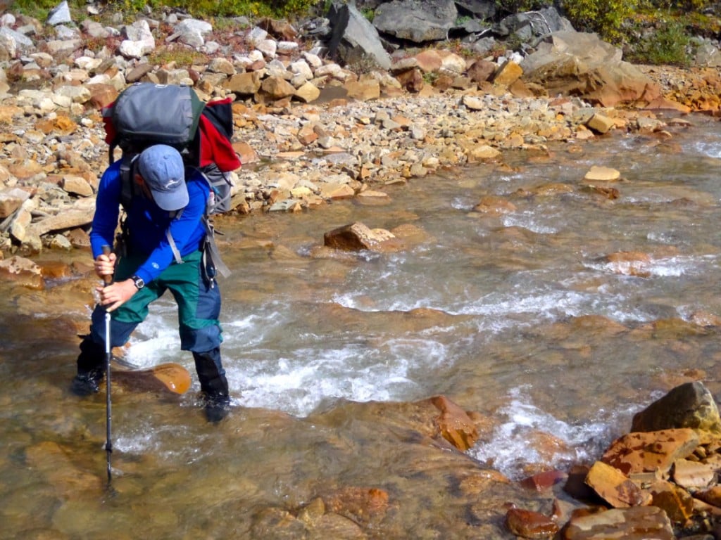 Person crossing a river using a trekking pole for balance