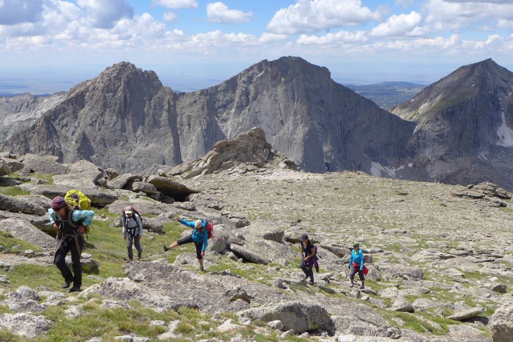 A group of five hikers go uphill with large cliffs in the background in the Wind River Range