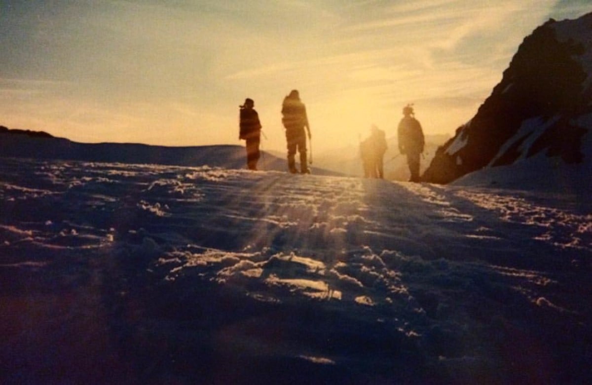 Four silhouetted figures on a snowfield in the mountains at sunset