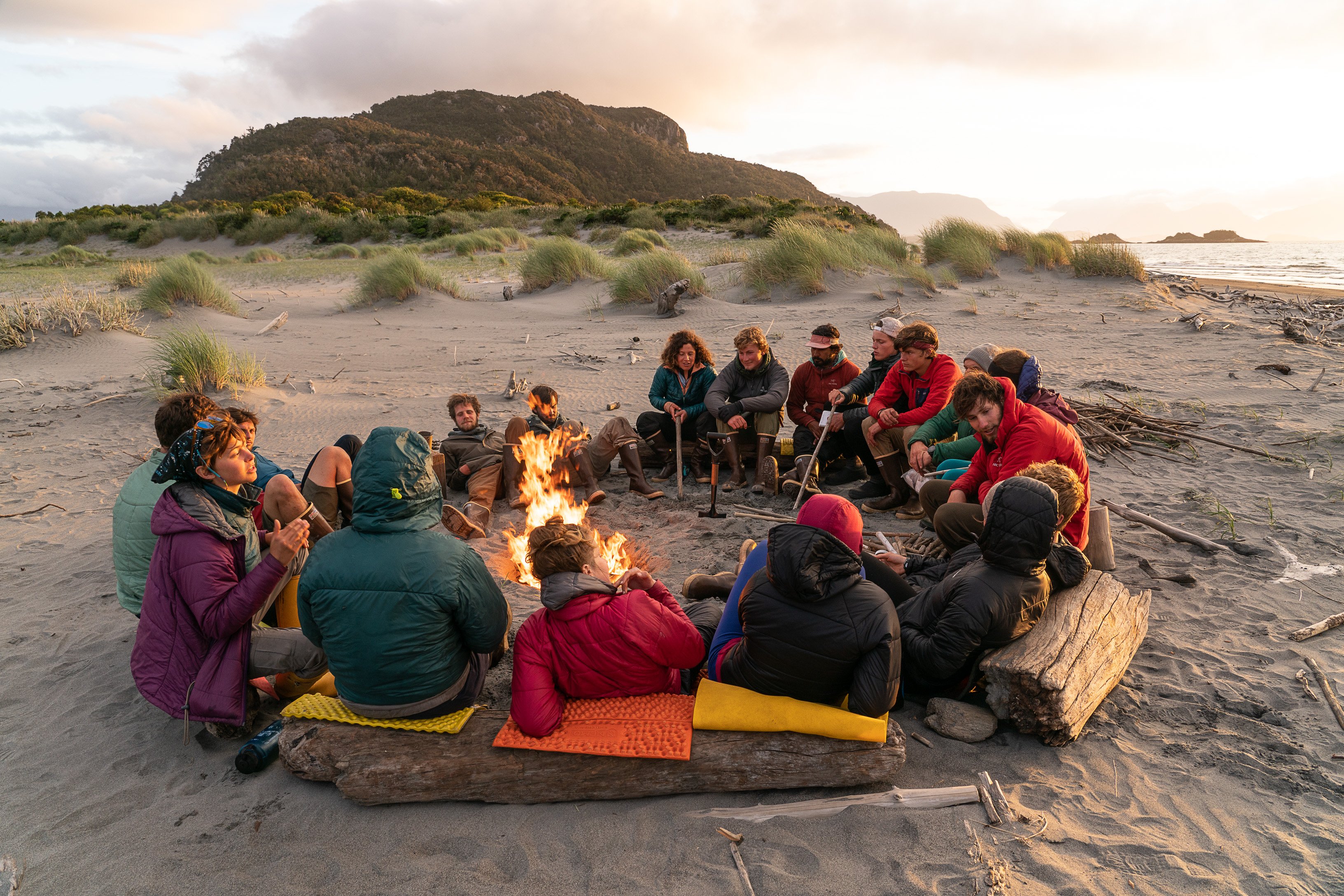 Group of students sitting in a circle around a fire on a beach in Patagonia at sunset