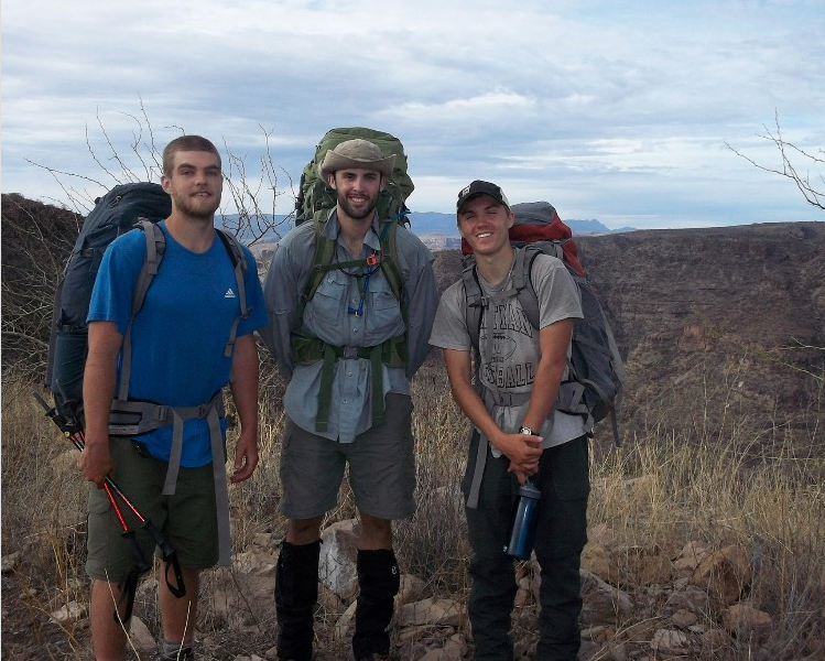 three NOLS students smile while backpacking