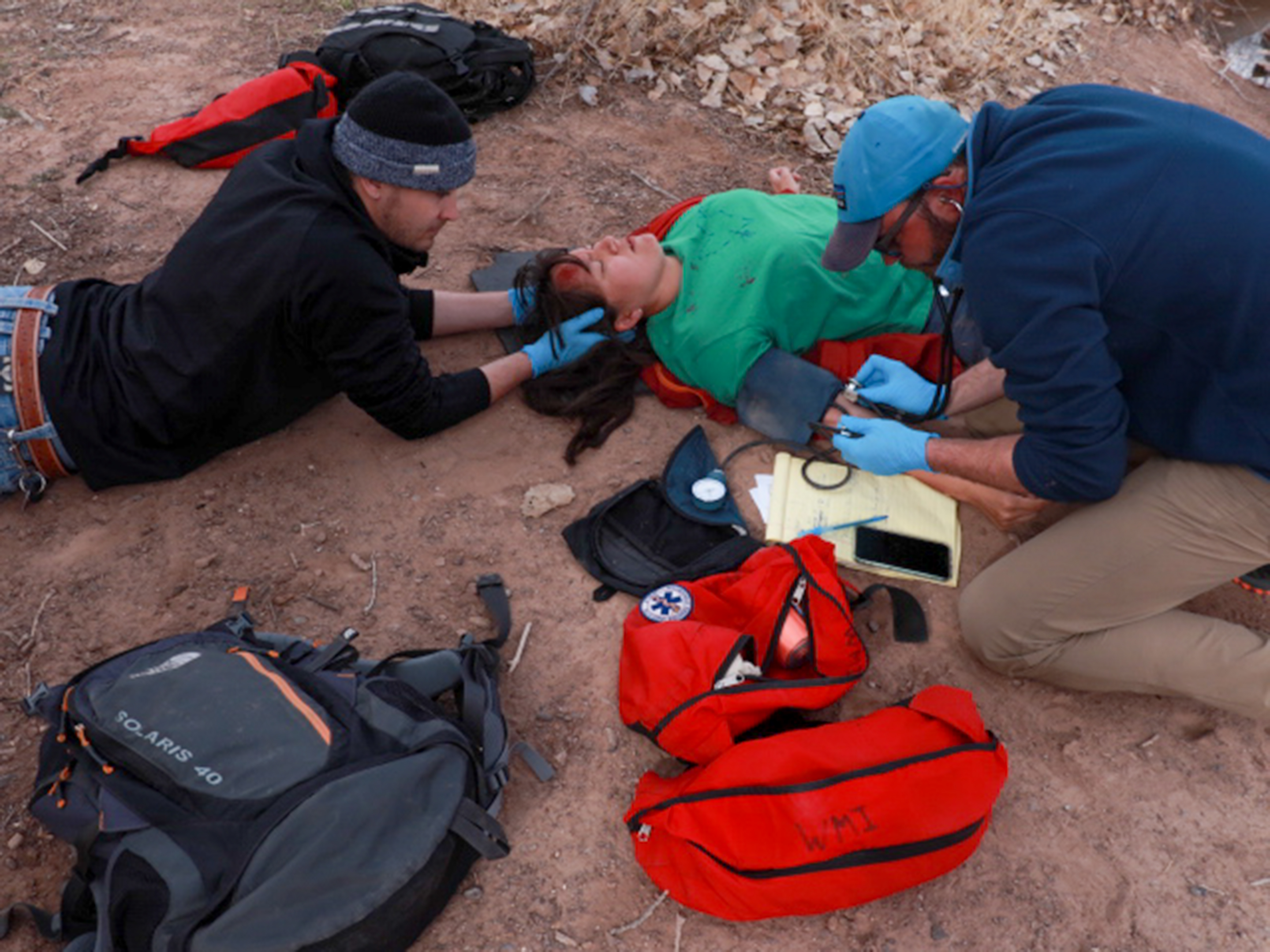 Two rescuers stabilize an unconscious patient's head and check her blood pressure.