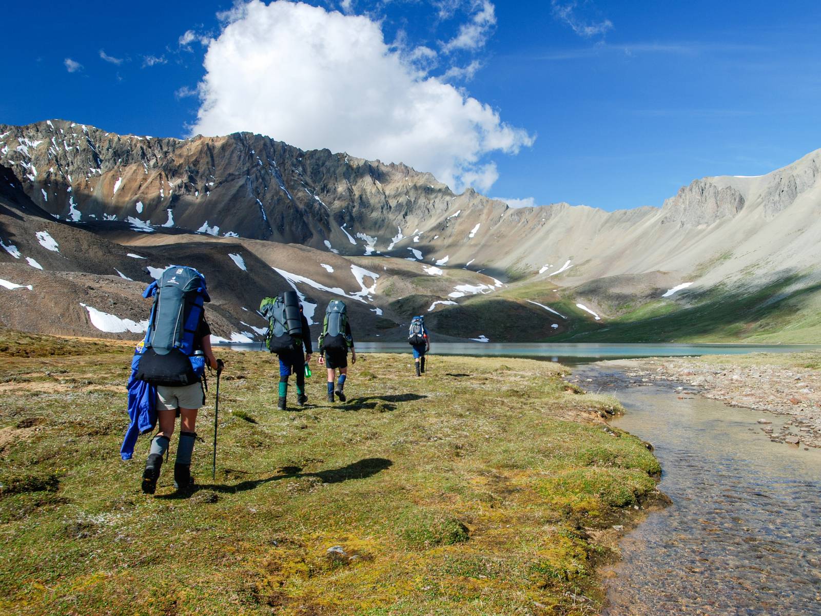 Group hiking across a green valley toward an alpine lake on a sunny day in Alaska